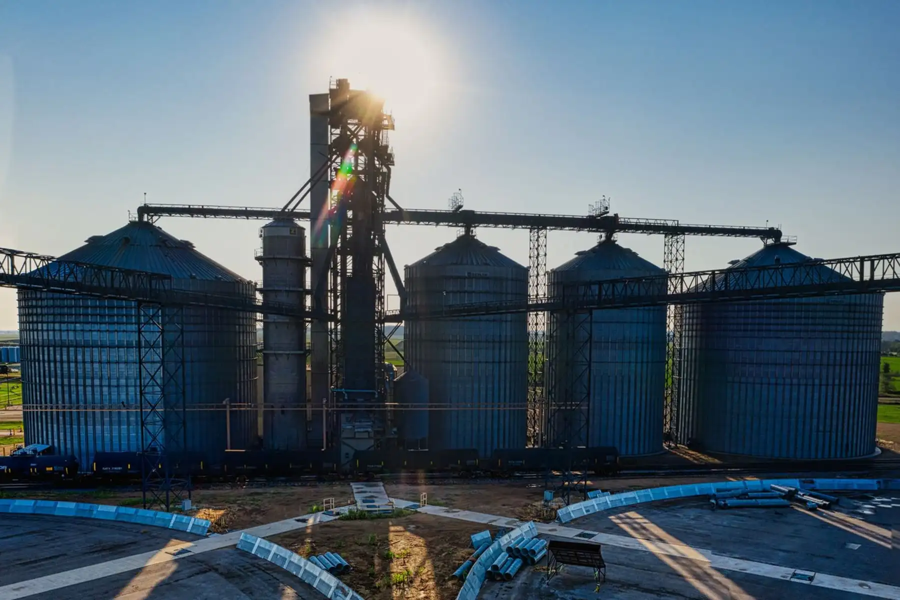 Bateria de silos metálicos com torre de elevador e correias de movimentação de grãos.